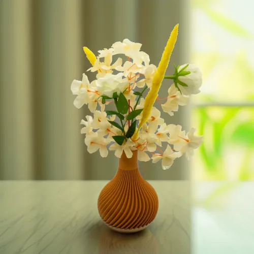 Een bruine vaas met decoratieve groeven, gevuld met witte en gele bloemen, staat op een marmeren tafel met een wazige achtergrond.