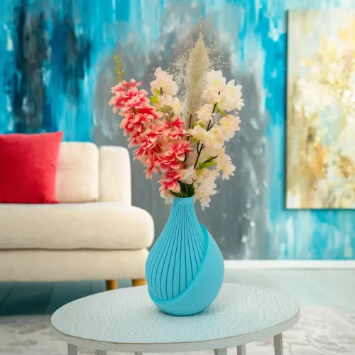 Een blauwe vaas met roze en witte bloemen staat op een tafel voor een beige bank met een rood kussen, tegen een blauwe achtergrond.
