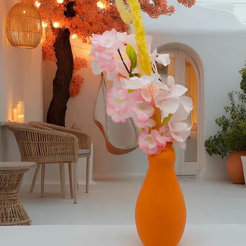 Oranje vaas met roze en witte bloemen in een sfeervol ingerichte ruimte met een hangstoel, een rieten stoel, een gekleurd boompje en zachte verlichting.