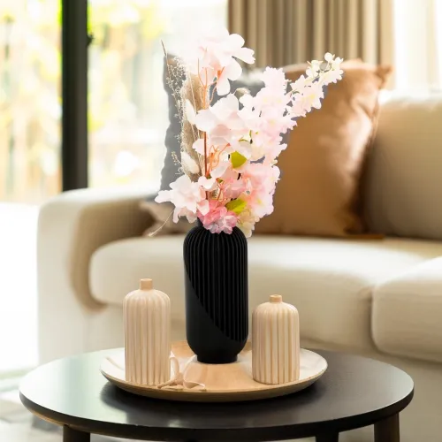 Zwarte vaas met roze bloemen op een dienblad, op een salontafel in een moderne woonkamer.