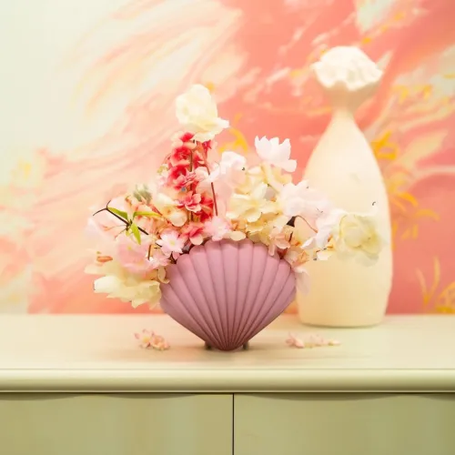 Roze vaas met pastelgekleurde bloemen, geplaatst op een lichtgekleurde kast tegen een roze achtergrond.