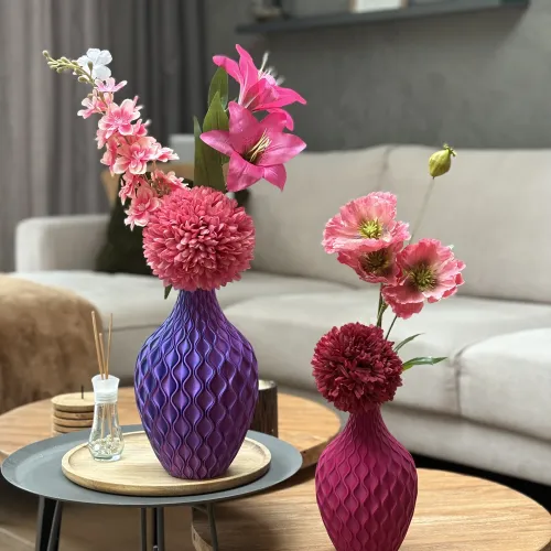 Twee golvende vazen met roze bloemen op houten tafeltjes in een moderne woonkamer met grijze bank op de achtergrond.